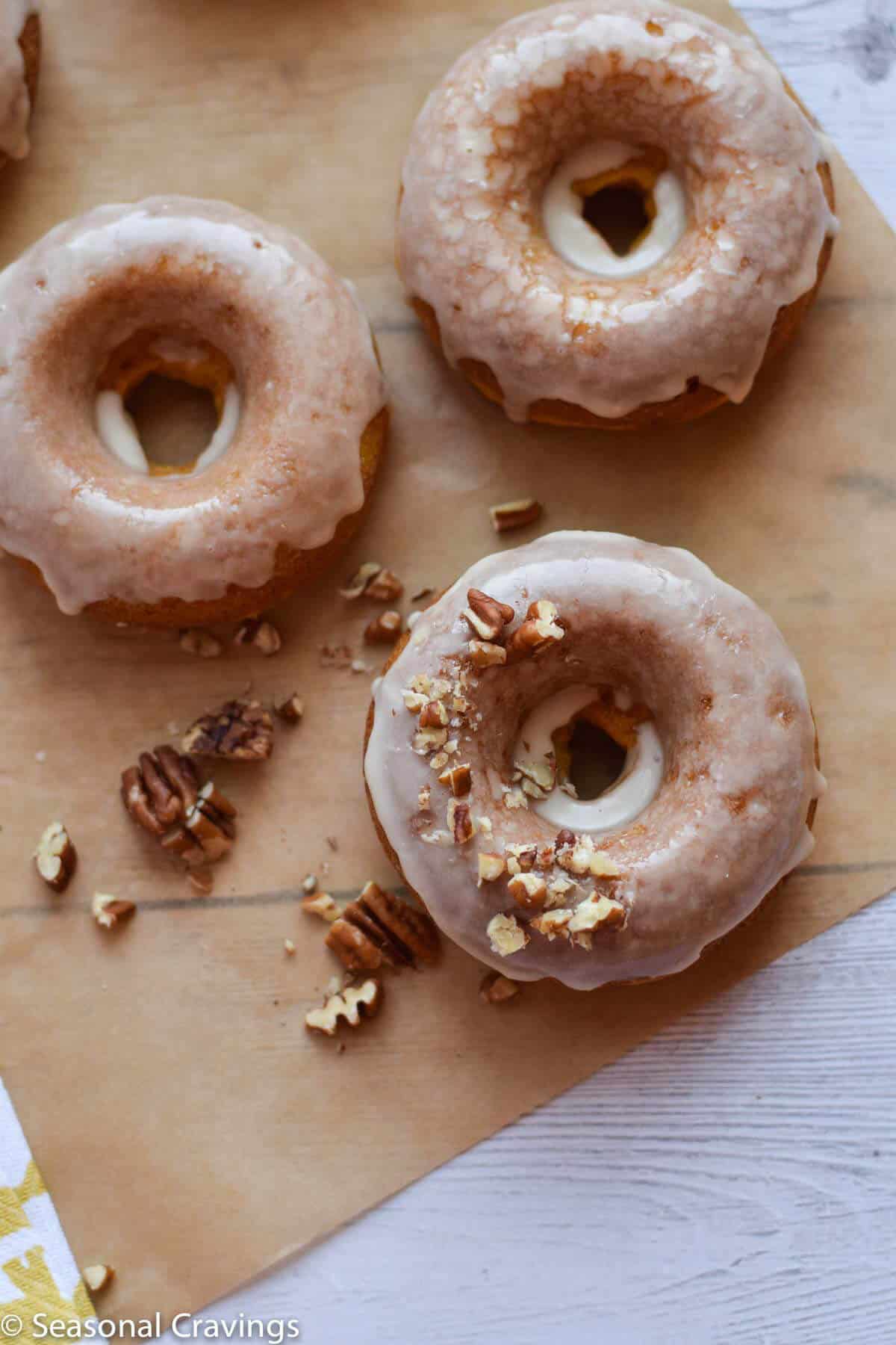 Easy Gluten Free Pumpkin Doughnuts light flaky and topped with pecans and frosting on brown parchment