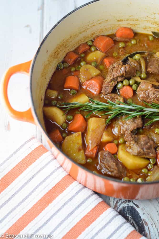 Apple Cider Beef Stew with carrots, potatoes, peas and rosemary in an orange pot