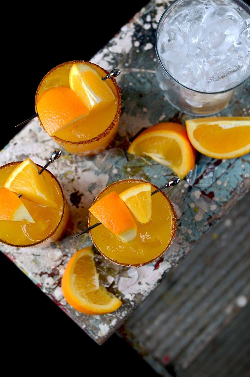 Orange-Turmeric-Margaritas in three glasses with oranges on the side