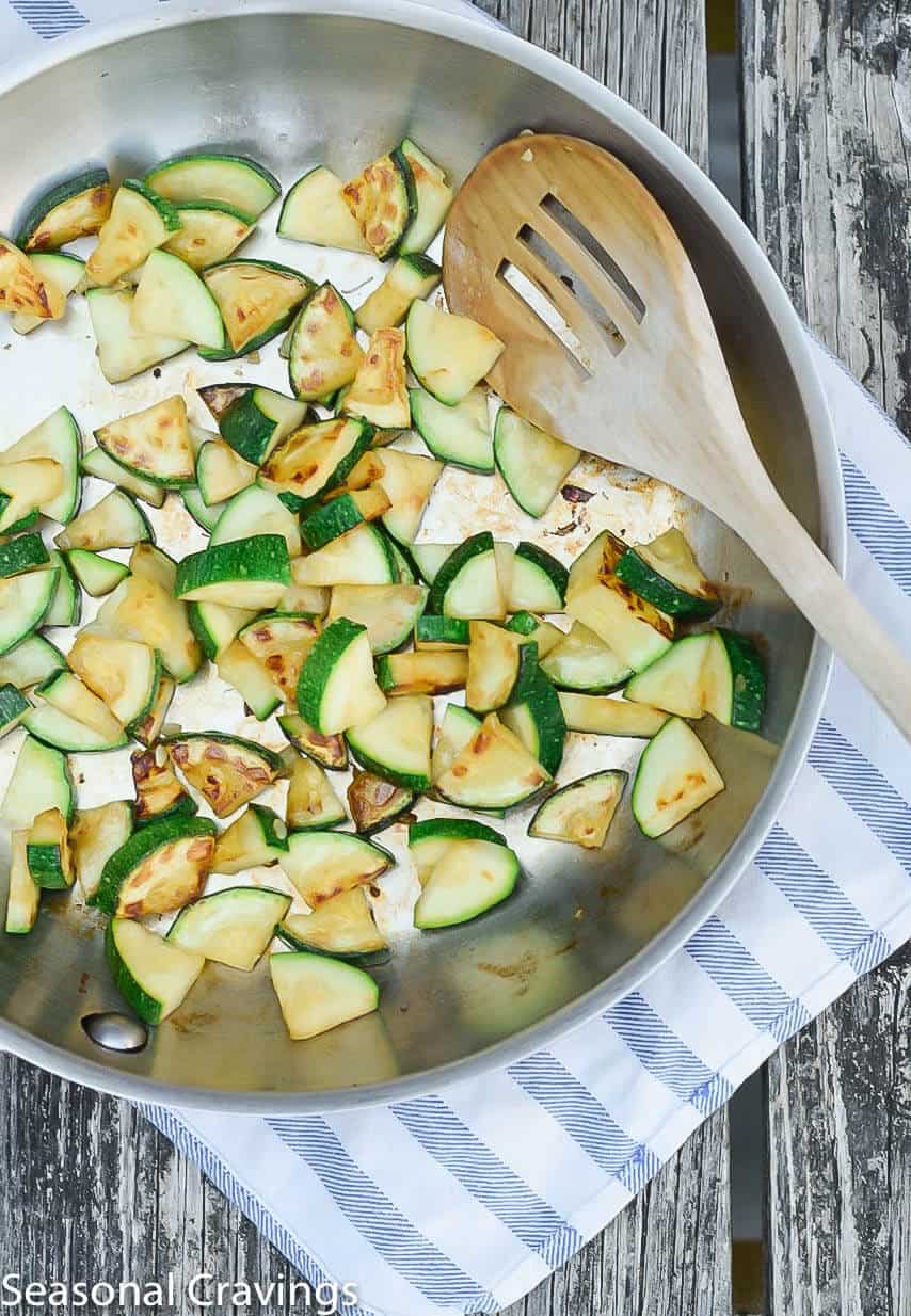 Sauteed zucchini in a skillet with a wooden spoon