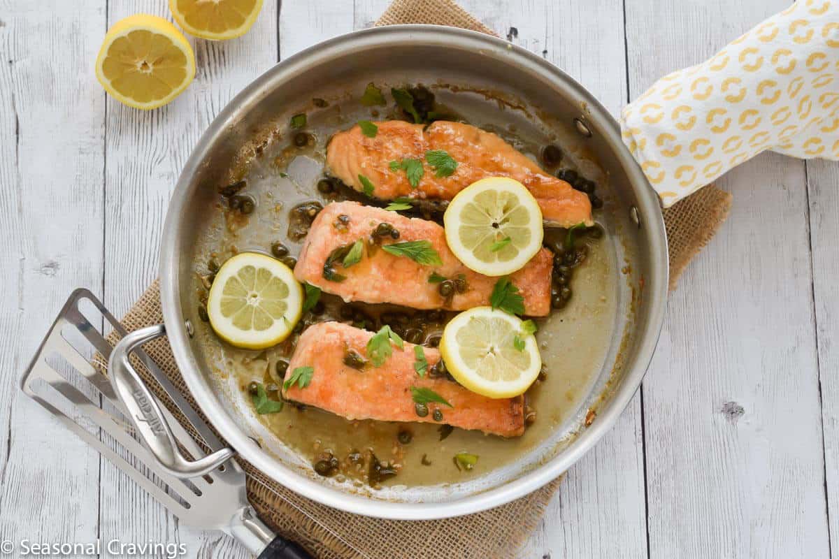 Gluten Free Salmon Piccata with lemon, capers and parsley in a skillet on white table