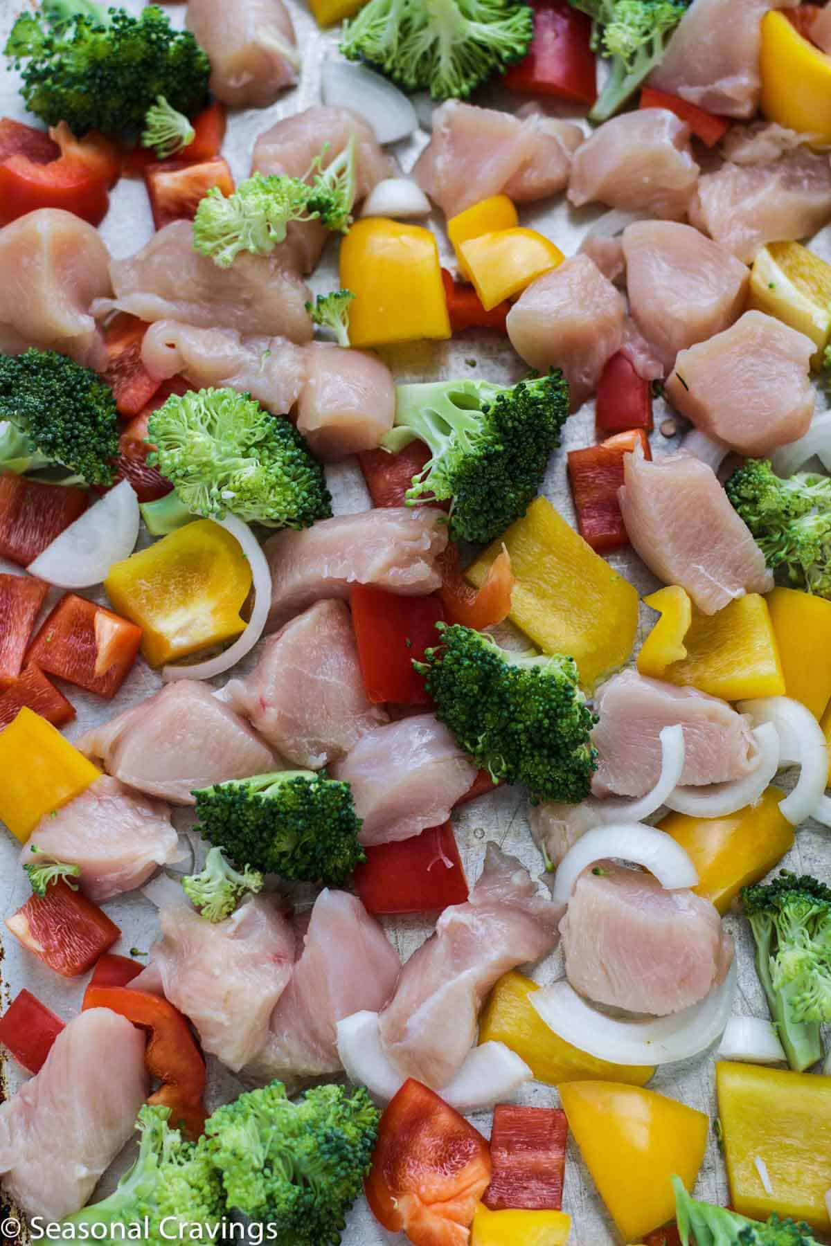 uncooked Chicken Stir Fry before on a sheet pan with broccoli and peppers