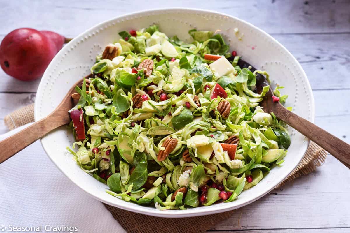 Brussel Sprout Salad with Pear and Pomegranate in a bowl with two wooden spoons