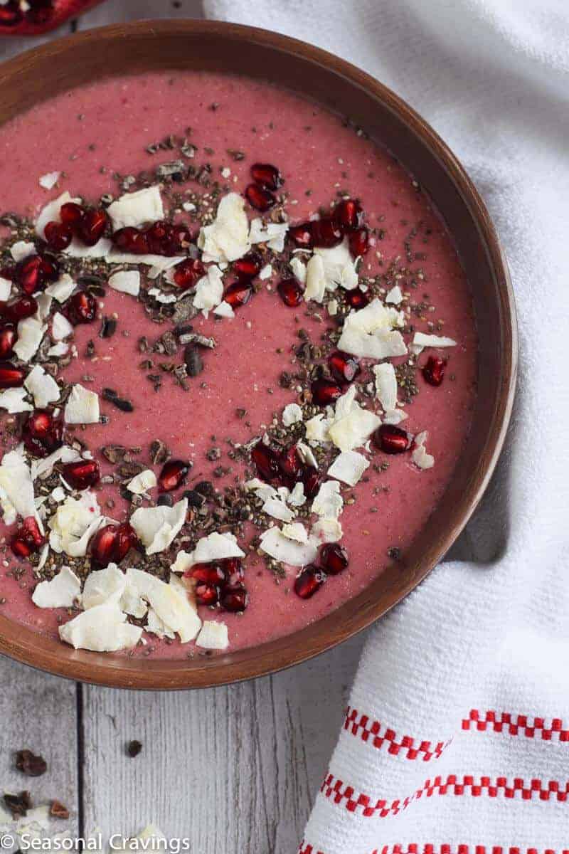 pomegranate smoothie in a brown bowl with toppings