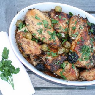 Roasted chicken with olives and parsley on a wooden table.