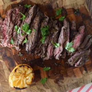 A marinated skirt steak on a wooden cutting board with lemon wedges.