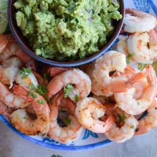 Shrimp and guacamole on a plate with a bowl of guacamole.