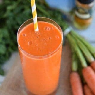 Carrot juice in a glass with carrots and a straw.