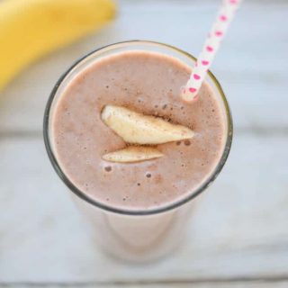 A chocolate protein smoothie with a straw and bananas.