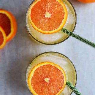 Two glasses of orange juice with a straw, transformed into refreshing orange spritzers.