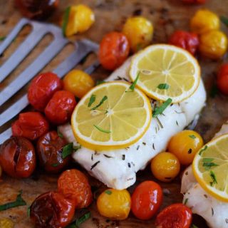 Skinny roasted cod with lemon and tomatoes on a baking sheet.