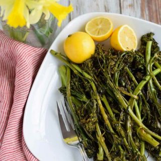 Roasted broccolini on a white plate with lemon wedges.