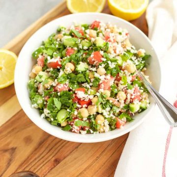 A bowl of chickpea and cauliflower Tabbouleh salad on a wooden cutting board.
