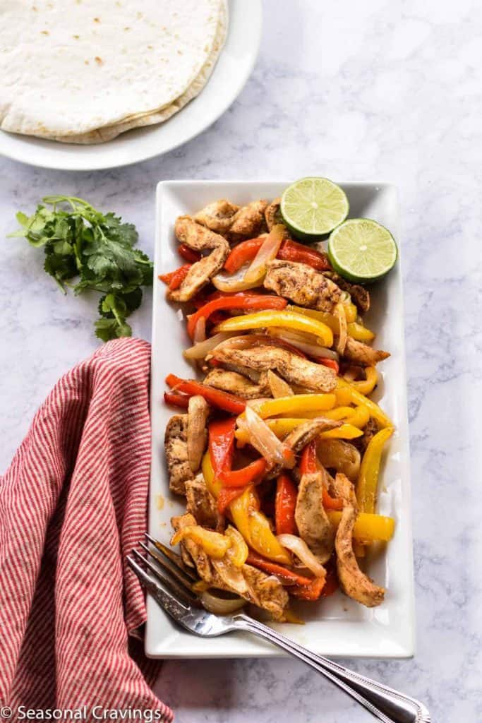 Sheet Pan Chicken Fajitas on a white plate with limes