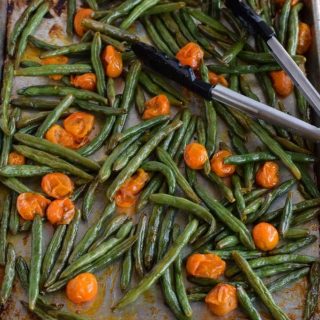 Oven roasted green beans and tomatoes on a baking sheet.