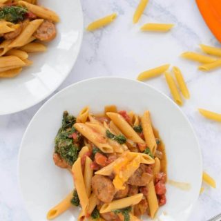 Two bowls of pasta with sausage and spinach cooked in one pot.