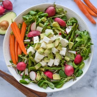 A green salad with radishes, carrots and tofu in a white bowl.