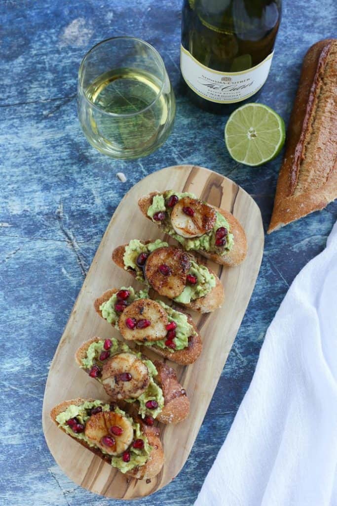 Crostini with Scallops and Avocado on wooden board with glass of wine and lime
