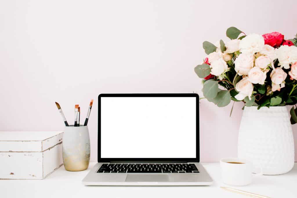 Home office desk with blank screen laptop, beautiful roses and eucalyptus