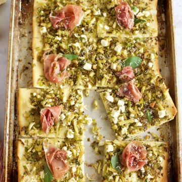 A prosciutto pizza with pistachios on a baking sheet is a delicious and unique twist on traditional pizza. The combination of the salty prosciutto and the crunchy pistachios creates a perfect