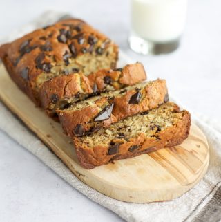 Gluten free chocolate chip banana bread on a cutting board with a glass of milk.