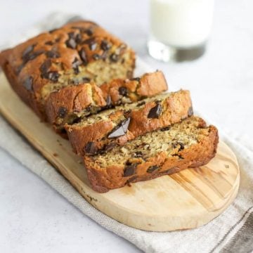 Gluten free chocolate chip banana bread on a cutting board with a glass of milk.