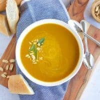 Two bowls of instant pot pumpkin soup on a wooden cutting board.