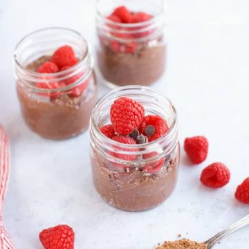 Three jars of chocolate chia pudding with raspberries and chocolate chips.