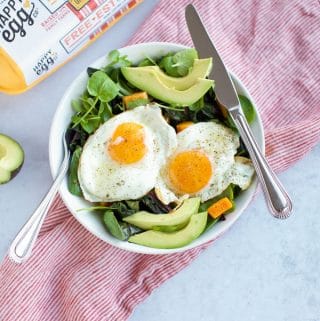 A protein bowl with eggs and avocado, topped with greens.
