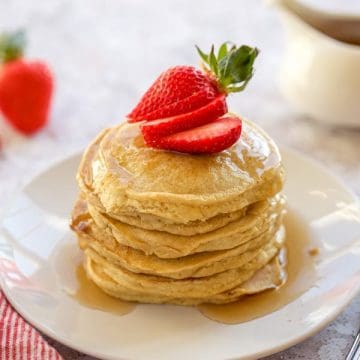 A stack of gluten-free pancakes with syrup and strawberries on a plate.