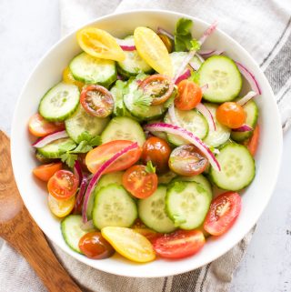A bowl of Cucumber and Tomato Salad with a wooden spoon.