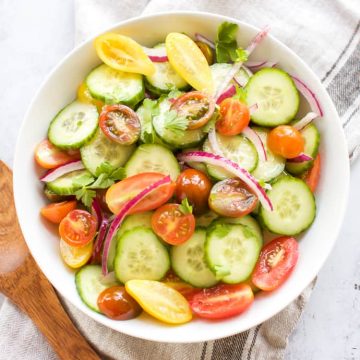 A bowl of Cucumber and Tomato Salad with a wooden spoon.