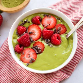 A bowl of matcha smoothie with strawberries and raspberries.
