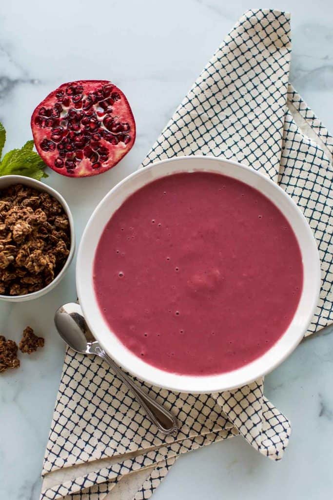 smoothie in a white bowl with pomegranate on the side