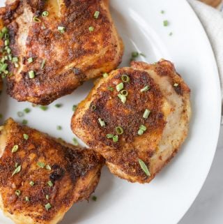 Four chicken thighs on a white plate.