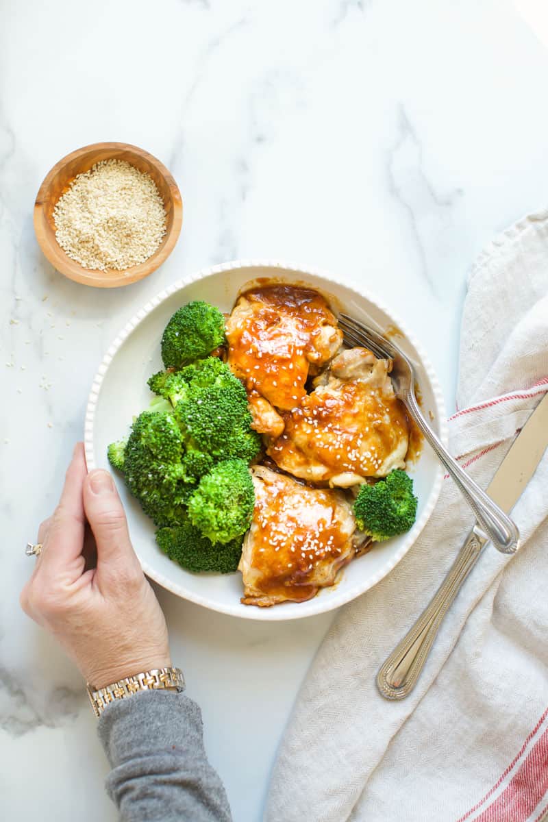 An Instant Pot chicken teriyaki recipe being prepared by a person holding a bowl of chicken and broccoli.