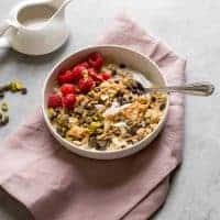 A bowl of granola topped with raspberries and pistachios.