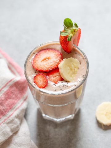 strawberry smoothie in a glass with banana slices on the side