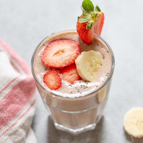 strawberry smoothie in a glass with banana slices on the side