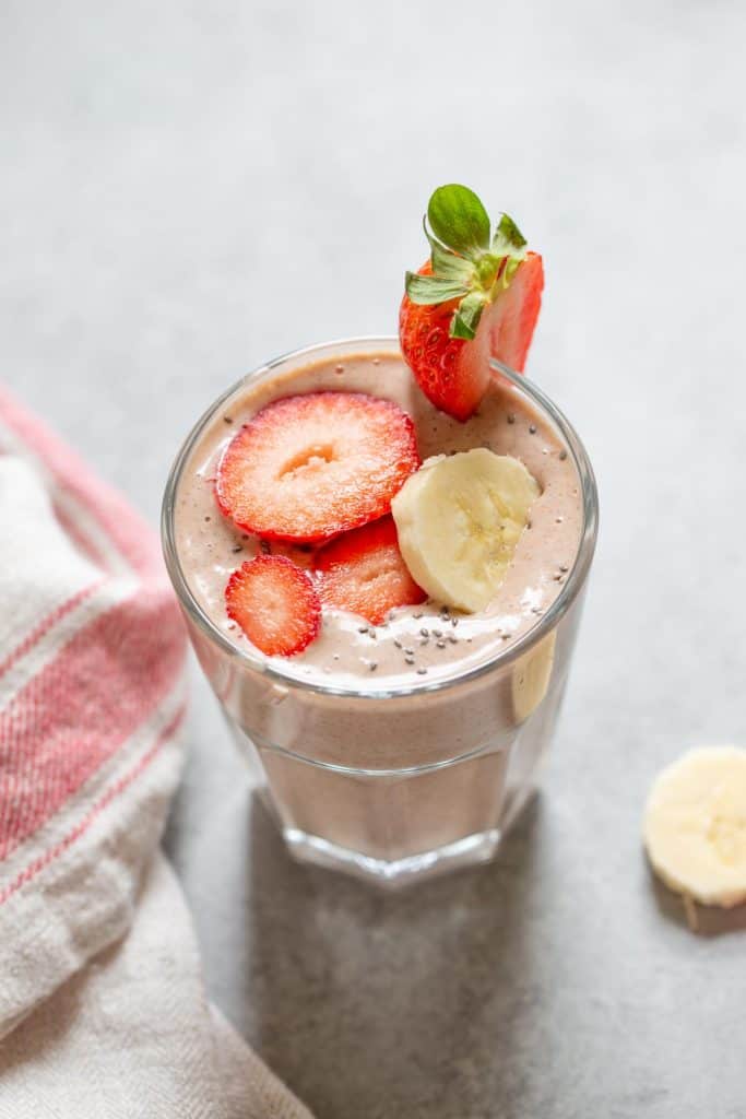 peanut butter strawberry banana smoothie in a glass with banana slices on the side