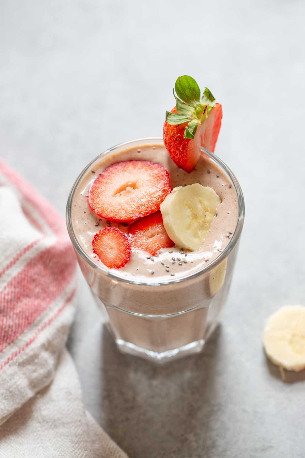 strawberry smoothie in a glass with banana slices on the side