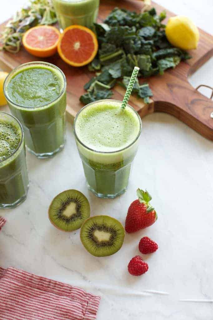 3 green smoothies in glasses with fruit on the side
