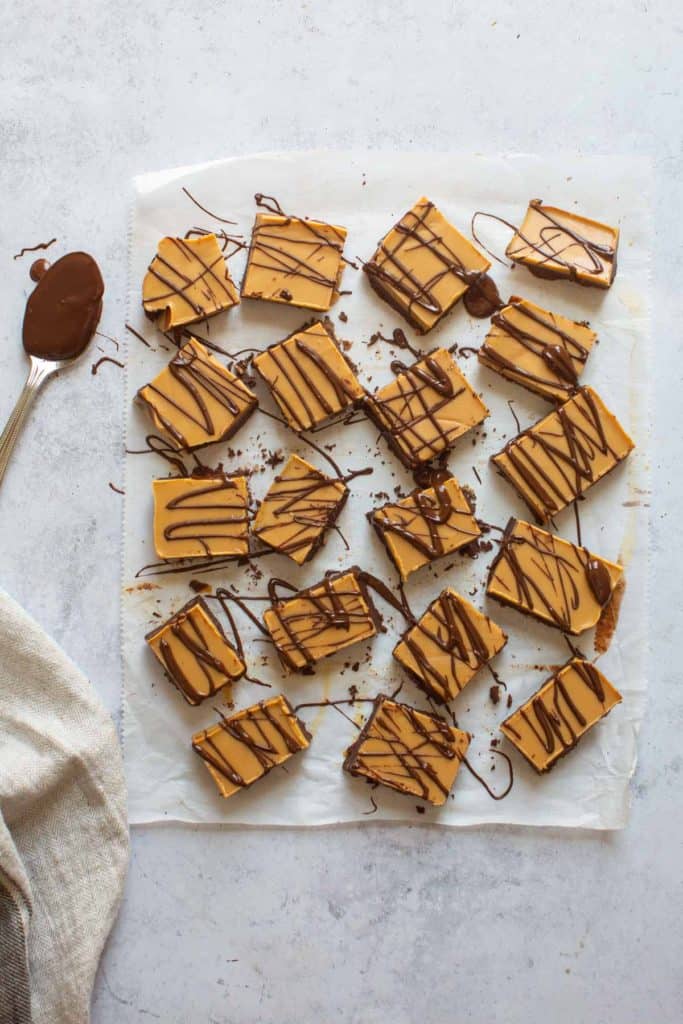 pieces of chocolate peanut butter fudge with chocolate drizzle on parchment paper