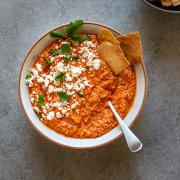 A bowl of roasted red pepper hummus with feta and pita chips.