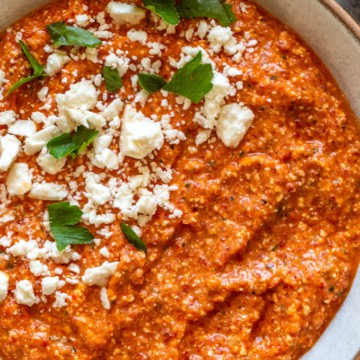 A bowl of roasted red pepper dip with feta cheese and tortilla chips.