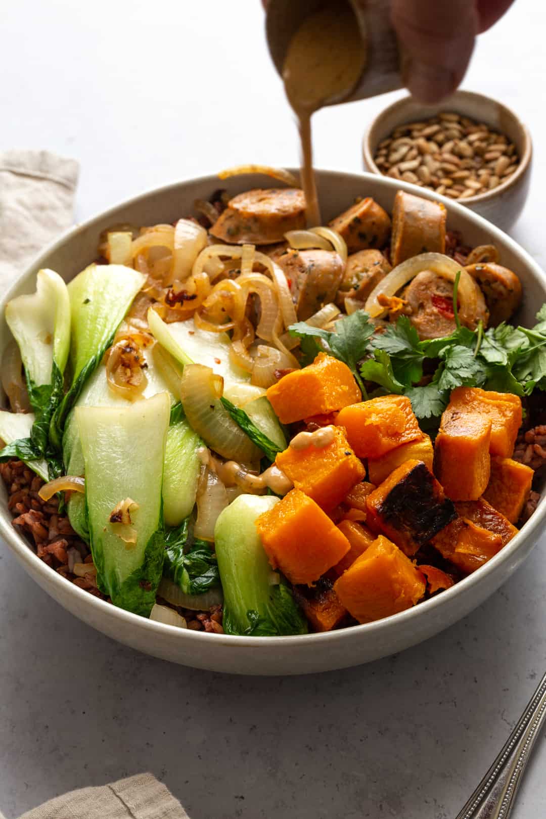 A person is pouring a Creamy Tahini Dressing on a bowl of vegetables.