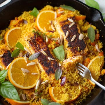 Turmeric salmon cooked with couscous and topped with oranges in a skillet.