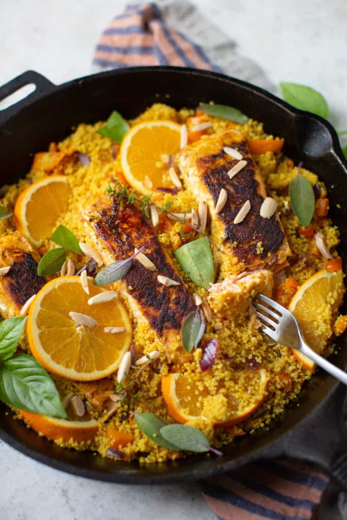 turmeric salmon with orange slices and couscous in a cast iron skillet