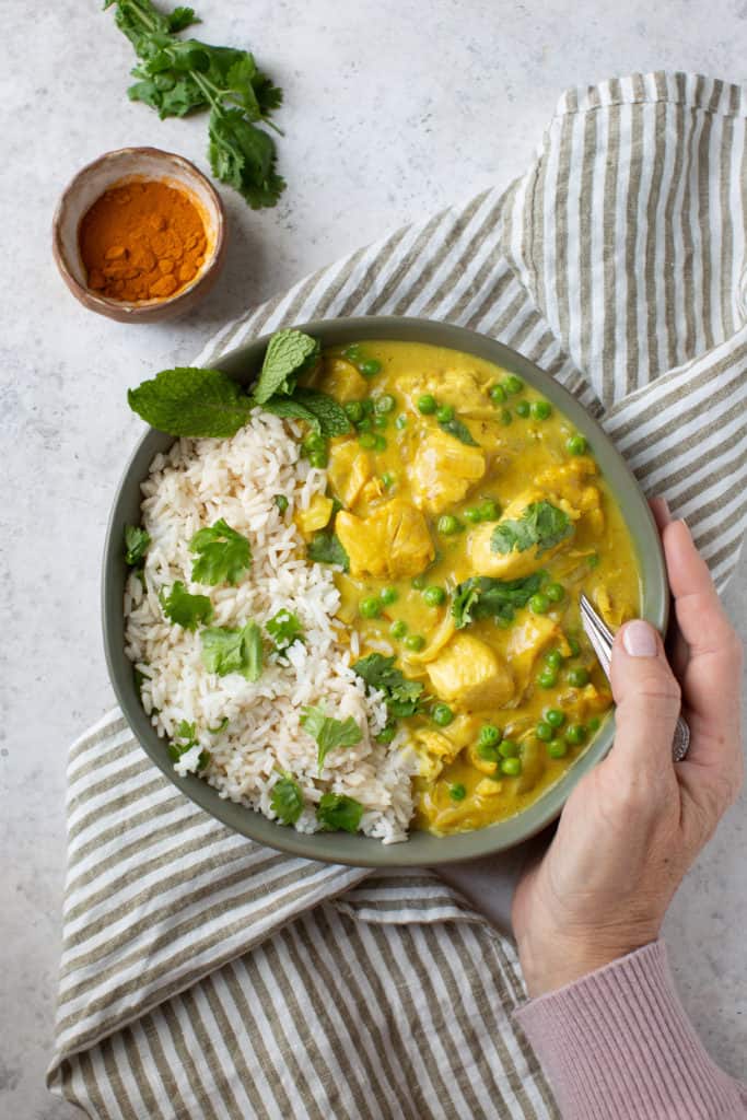 hand around bowl of chicken curry with rice