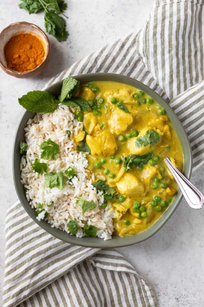 creamy curry chicken in a bowl with turmeric on the side